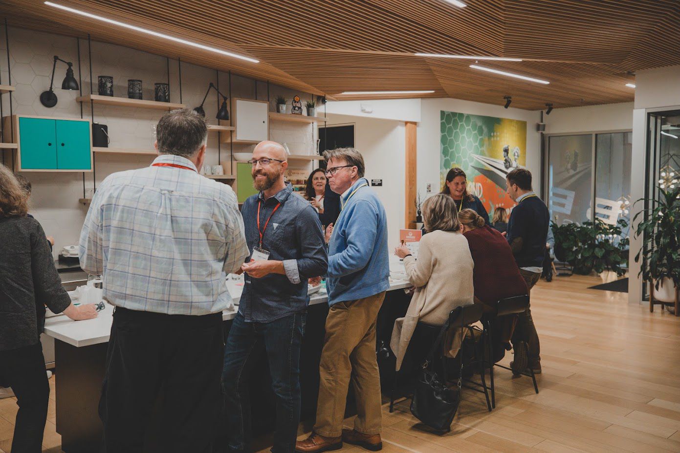People wearing name badges talk and laugh around a kitchen island at an event in a coworking space