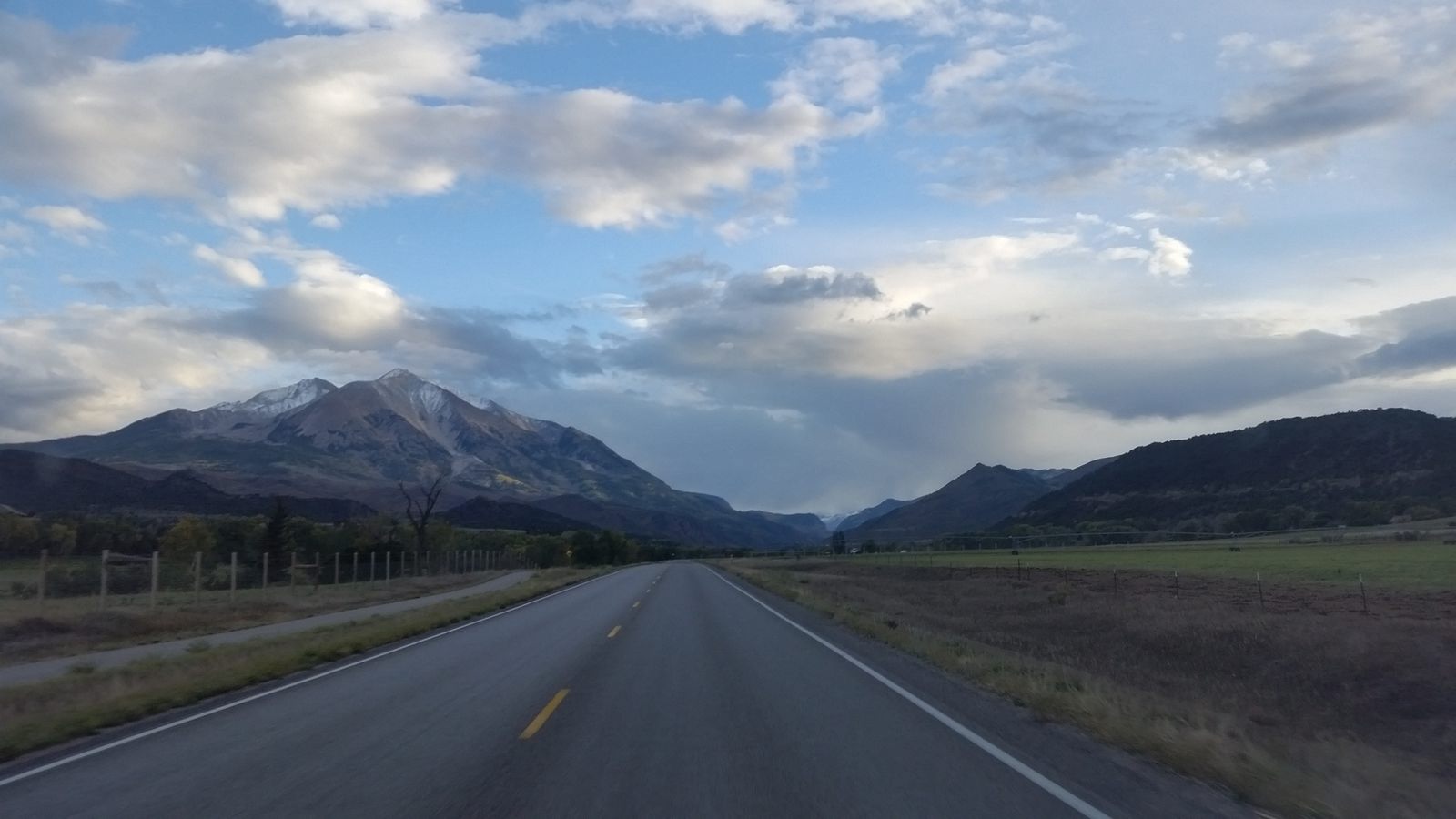 A two-lane road running toward Mt. Sopris under a partly cloudy sky
